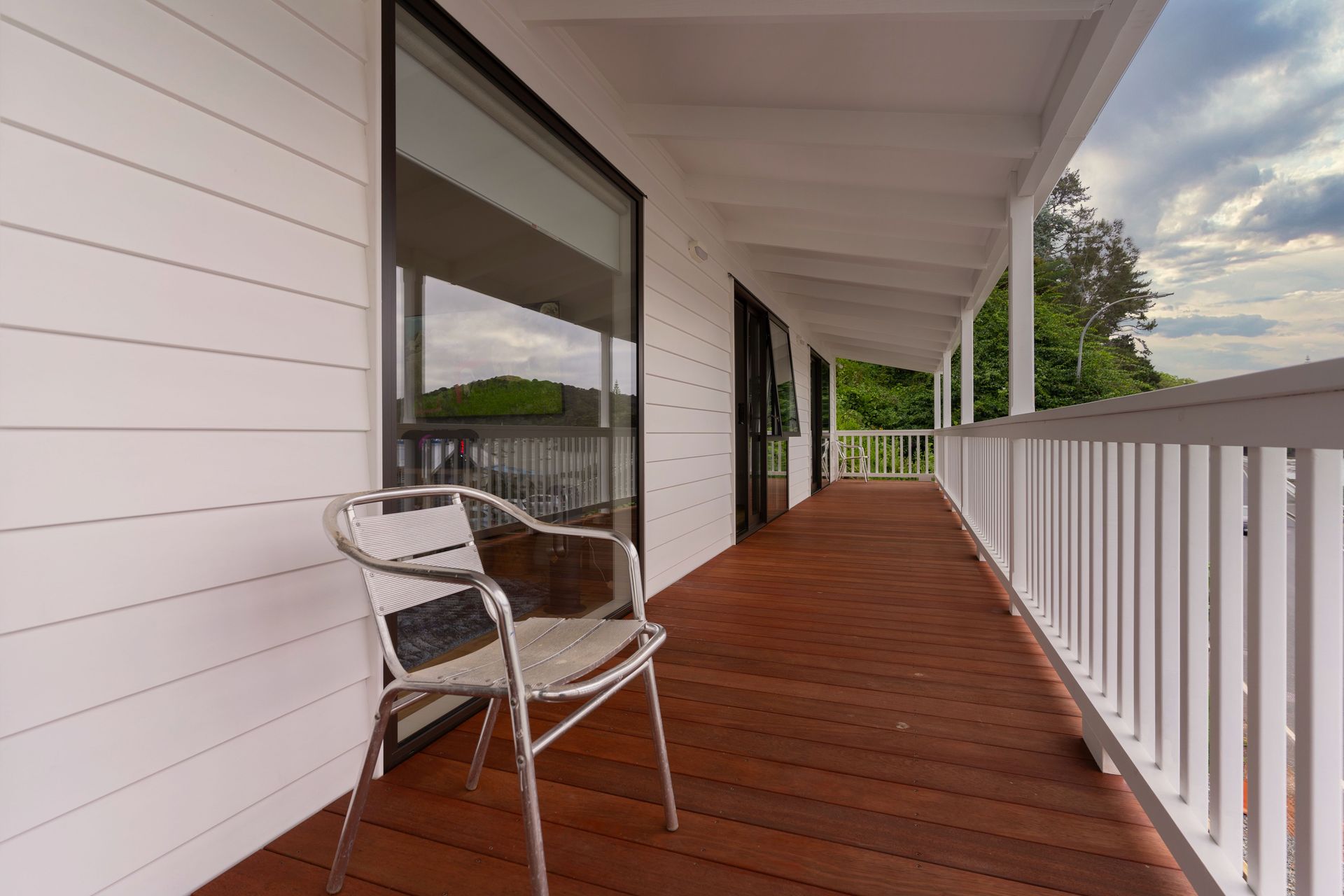 Contemporary wooden porch with metal chair, white facade, outdoor setting.